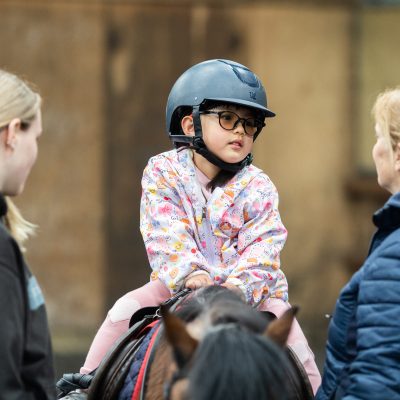 A young girl sits on top of a pony, listening intently to her instructor at Bourne Vale Stables in Aldridge near Birmingham