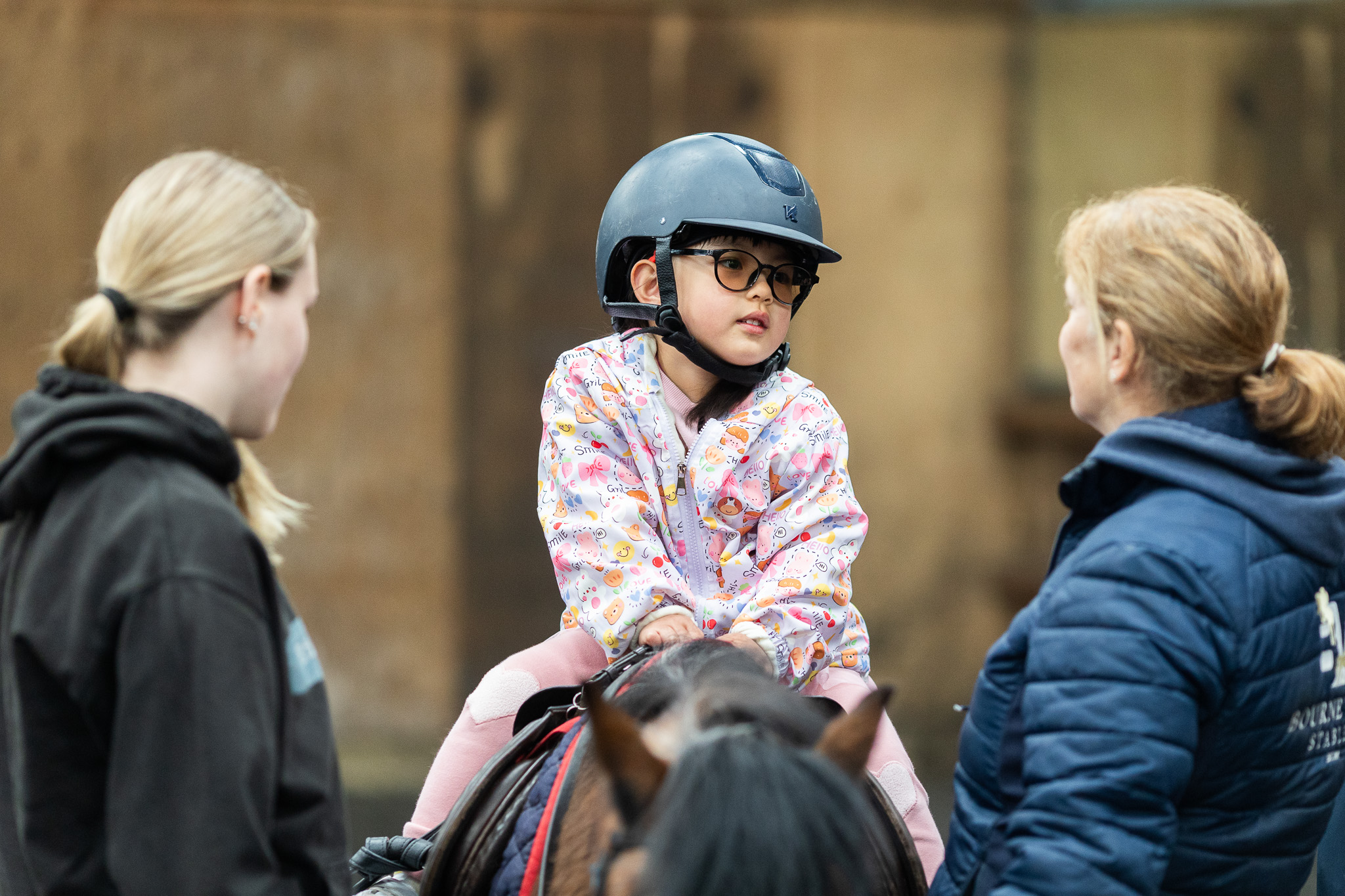 A young girl sits on top of a pony, listening intently to her instructor at Bourne Vale Stables in Aldridge near Birmingham