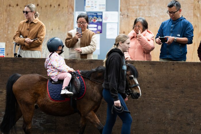 Parents and grandparents watch from the gallery as a small child is led past and a pony at Bourne Vale Stables near Birmingham