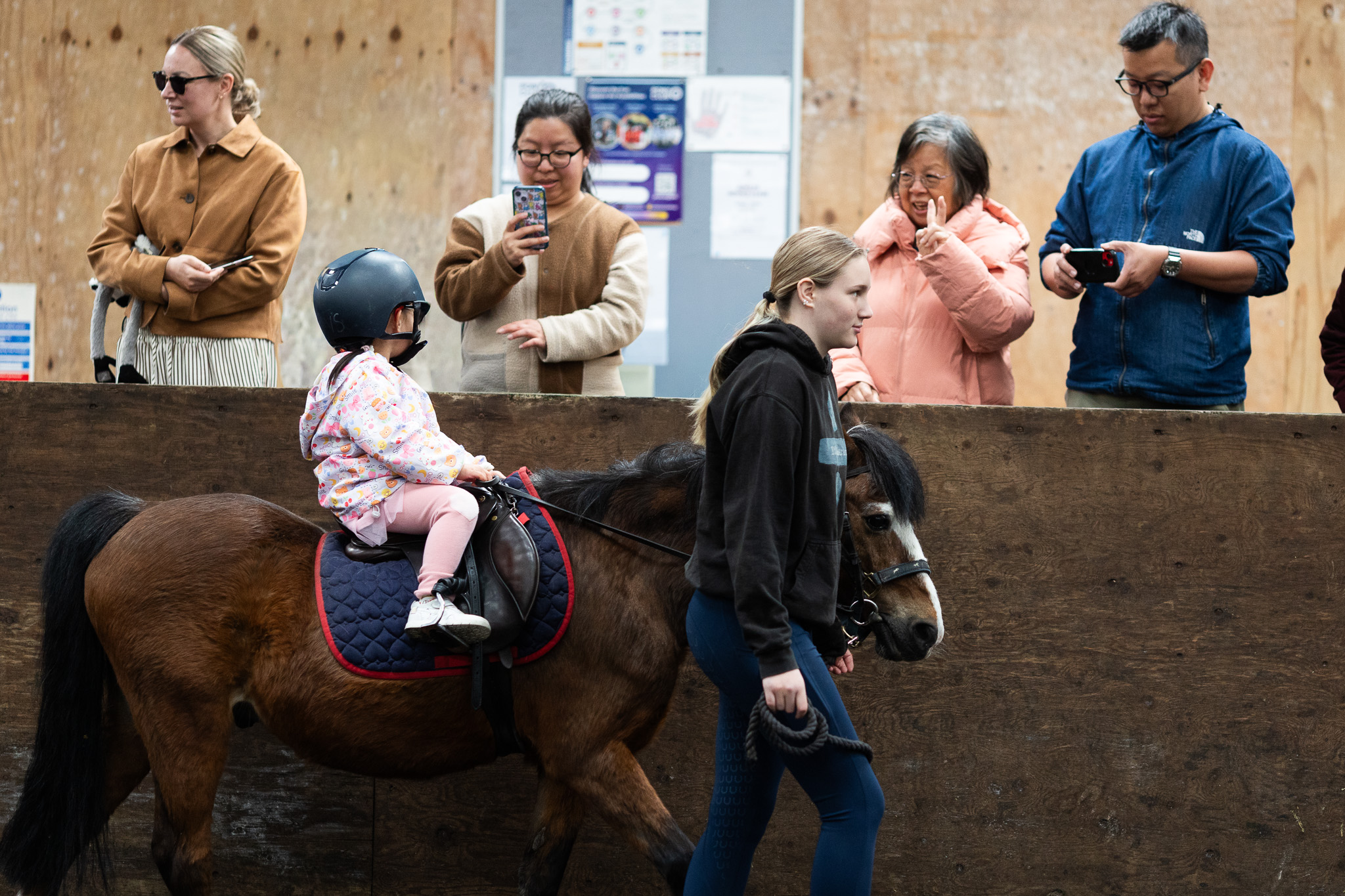 Parents watch on from the gallery as a young child walks past on a pony during a Tiny Tots session at Bourne Vale Stables