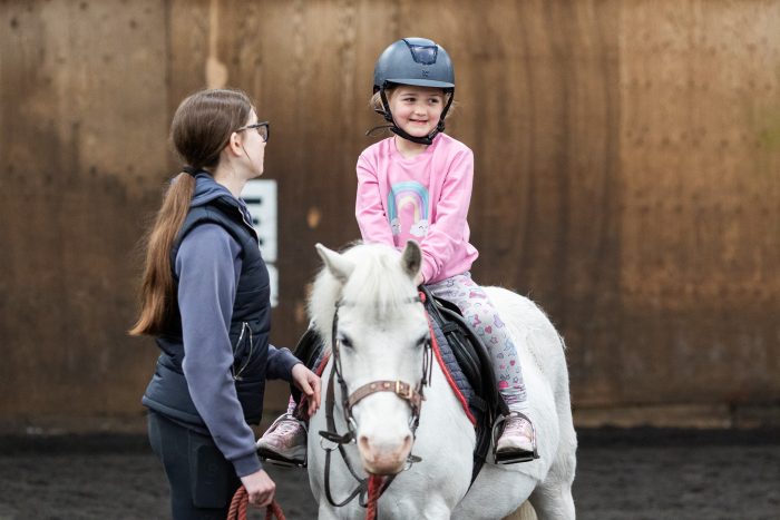 A young child smiling, sitting on a grey pony