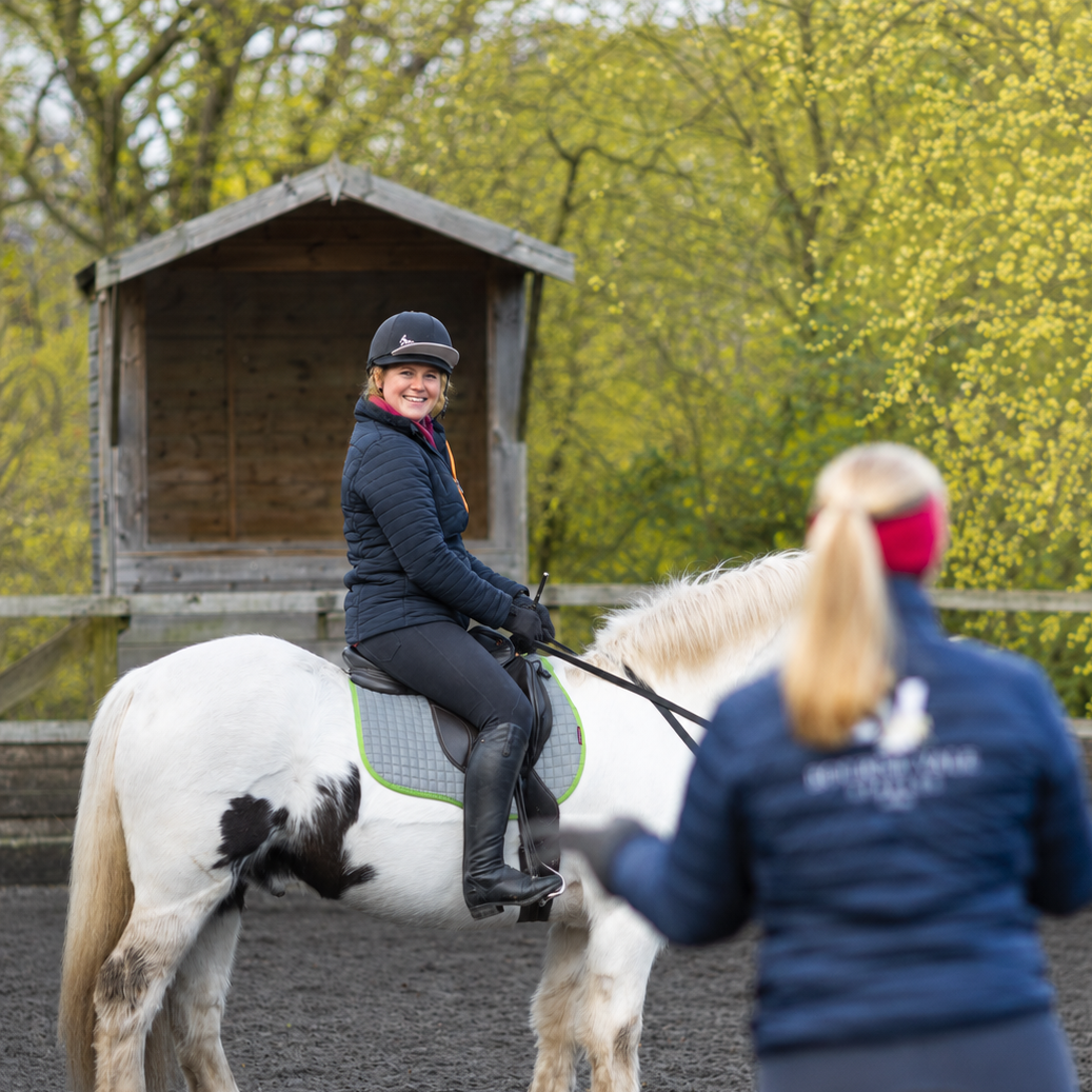 A beginner rider, sitting on a horse, smiles during a private riding lesson at Bourne Vale Stables near Birmingham
