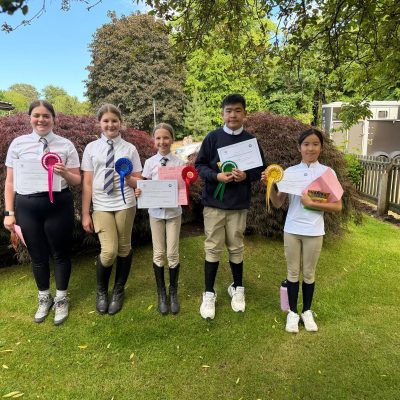 Pony club members holding pony club rosettes and certificates