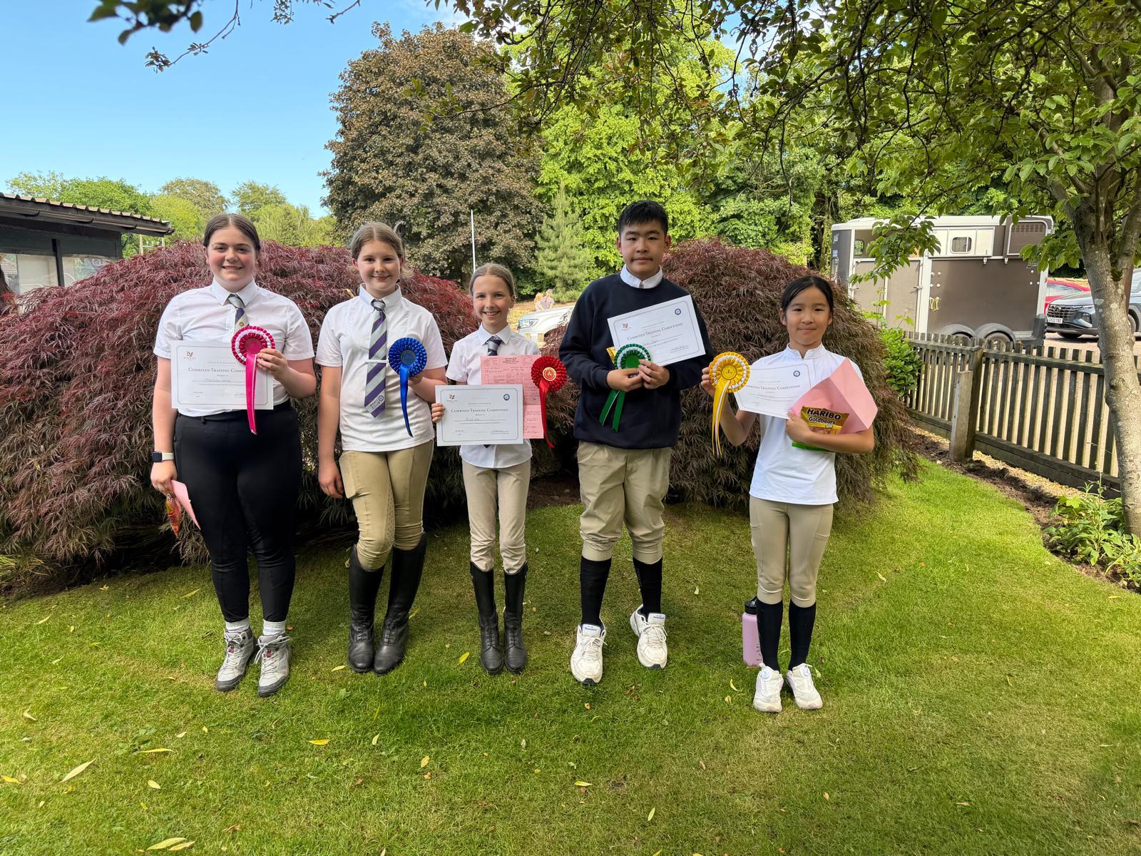 Pony club members holding pony club rosettes and certificates